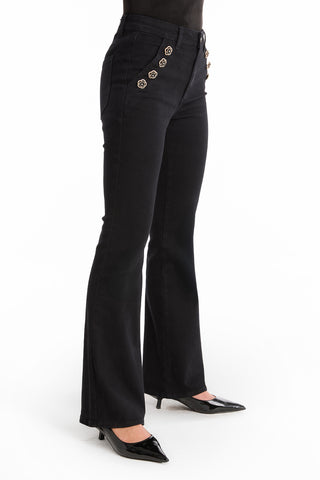 Wearing the Allegra Rose Jean - Black, a high-waisted bootcut style with rose buttons at the hip, paired with black pointed-toe heels and standing against a white background.