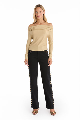 A woman stands facing forward against a white background, wearing the Victoria Shimmer Top in Gold off the shoulder, paired with black high-waisted pants with side button details and open-toed heels.