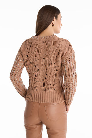 A woman faces away, wearing the Elea Crystal Knit Sweater in mocha with a leaf pattern and matching high-waisted pants. Her straight brown hair is tucked behind her ear against a white background.