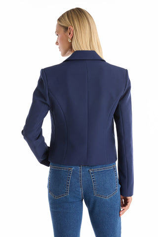A woman with straight blonde hair, wearing a navy Gabrielle Double Breasted Blazer and blue jeans, stands facing away from the camera against a white background.