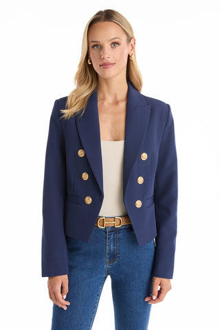 A woman with long blonde hair wears the Gabrielle Double Breasted Blazer - Navy with gold buttons, a beige top, and blue jeans. She faces forward against a plain white background.