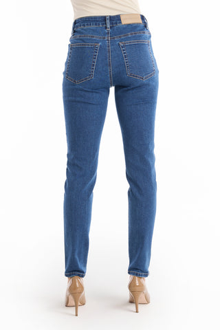 A person faces away, wearing the Layla Skinny Jean - Medium Blue—a high-waisted skinny jean in stretch denim with back pockets and a leather waistband patch—paired with beige high heels against a white background.