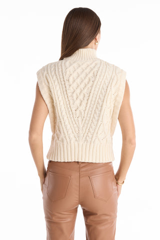 A woman with long brown hair, seen from behind, wears the Raina Cable Knit Button Sweater in Pearl and high-waisted light brown pants against a white background.