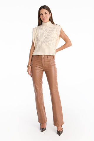 A woman poses in the Raina Cable Knit Button Sweater - Pearl paired with high-waisted brown leather pants and brown pointed-toe heels, standing against a plain white background.
