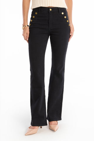 A person wearing the Allegra Bootcut Jean - Black with gold button details, paired with a cream sleeveless top, nude heels, and a gold bracelet, shown from shoulders down for a vintage flair.