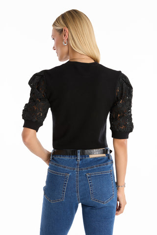 A woman with straight blonde hair wears the black Sylvie Lace Sleeve Top and blue high-waisted jeans, standing with her back to the camera against a white background.