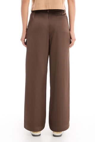 Person standing with their back to the camera, wearing Milan Satin Cargo Pant in Espresso, a tan top, and white shoes with light-colored soles. The background is white and uncluttered.