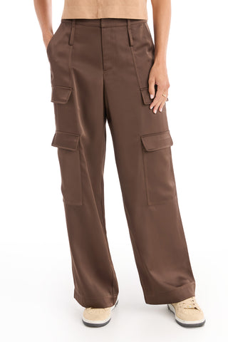 A person models the Milan Satin Cargo Pant in Espresso, featuring wide legs and large side pockets, paired with a tan top and beige sneakers against a white background.