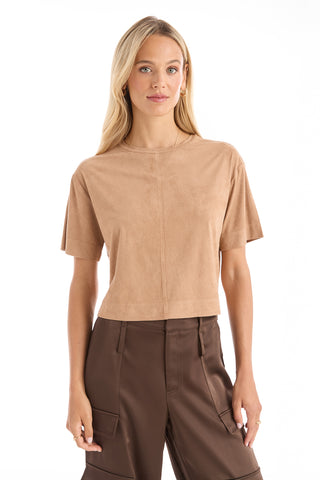 A woman with long blonde hair wears the Naya Suede T-Shirt - Cafe with a cropped fit and high-waisted brown cargo pants, standing against a white background.