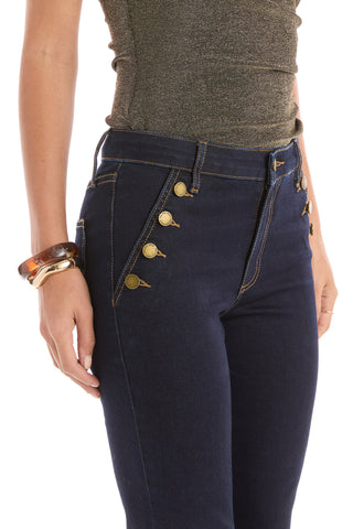A person wears the Allegra Bootcut Jean in indigo, which is high-waisted and flattering, paired with a fitted shimmery brown top and chunky brown and gold bracelets for a chic look.