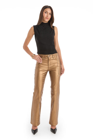 A woman stands confidently in a sleeveless black top, Aria Coated Flare Jean - Gold Metallic with a high-rise fit, chain belt, black heels, and gold bracelets against a white background.