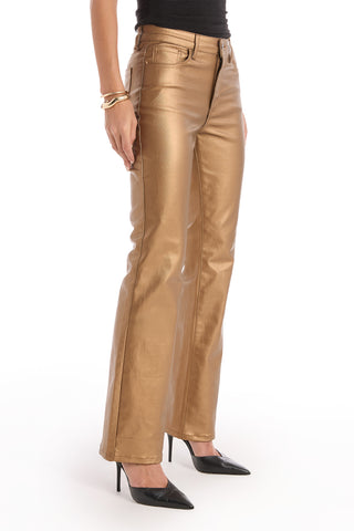 A person wearing gold metallic Aria Coated Flare Jeans, a black top, black pointed-toe heels, and bracelets stands against a white background.