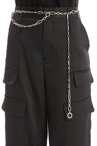 A person wearing black cargo pants with the Arden Chain Belt - Silver draped around their waist, hanging loosely and featuring a large metal washer at the end.