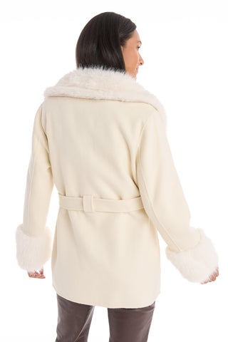 A person seen from behind wears the Isabel Fur Trim Coat - White, featuring wide faux fur trim on the collar and cuffs and a matching belt. Their straight dark hair and dark pants complete the outfit against a white background.