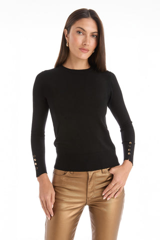 A woman with straight brown hair wears a fitted Marcela Knit Top - Black with gold button details on the sleeves and metallic gold pants. She faces forward with a neutral expression against a plain white background.