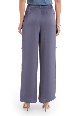 A woman, visible from the waist down against a white background, wears navy Milan Satin Cargo Pants with a wide-leg, high-waisted fit and side and back pockets, paired with nude heels.