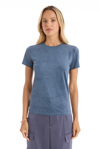 A woman with long blonde hair stands facing forward, wearing the Amaya Suede T-Shirt in blue and matching blue cargo-style pants, against a plain white background.