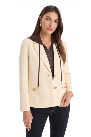 A woman with long brown hair wears the Kara Dickey Blazer in Pearl/Espresso over a brown hoodie and dark jeans. She stands against a white background, looking at the camera with a neutral expression.