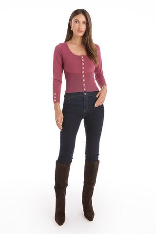 A woman with long brown hair stands facing forward in the Edie Knit Top - Sangria, paired with dark high-waisted jeans and knee-high dark brown boots, posed against a white background with a neutral expression.