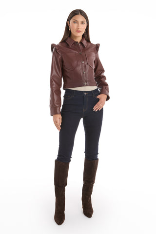A woman faces forward in the Chantal Ruffle Sleeve Leather Jacket – Espresso, paired with dark blue jeans and knee-high dark brown boots. With long, straight hair and a neutral expression, she models this perfect fall statement piece against a white background.