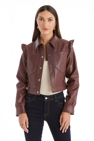 A woman with long brown hair wears the Chantal Ruffle Sleeve Leather Jacket in Espresso—a chic fall statement piece—paired with a white top and dark jeans, standing against a white background.