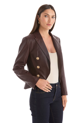 A woman wears the Gabrielle Leather Double Breasted Blazer in Espresso with gold buttons, a beige top, and dark jeans, standing and looking at the camera against a white background.