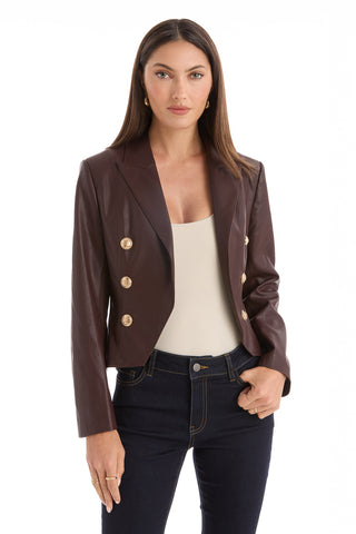 A woman with long brown hair wears the Gabrielle Leather Double Breasted Blazer in Espresso over a cream top and dark jeans, standing against a plain white background.