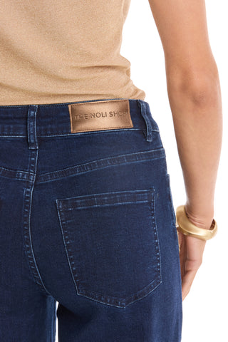 Wearing the Rocco Gold Embellished Jean - Indigo with a tan top and gold bracelet, shown from the waist down and behind.