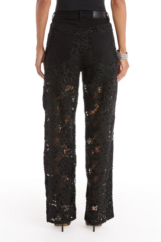 A person wearing the Celeste High Rise Jean - Black stands with their back to the camera, styled with a black top, heels, and silver bangles for a chic, modern silhouette.