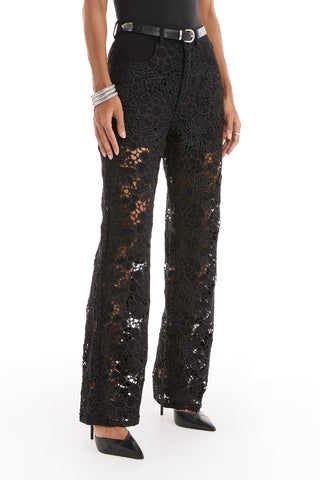 A person wears the Celeste High Rise Jean in black, styled with a black belt, pointed-toe heels, and silver bracelets, standing against a white background.