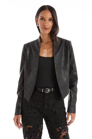 A woman with long dark hair wears the Yasmin Leather Jacket - Black over a matching black top, belt, and asymmetrical-hem lace pants. She stands facing forward against a white background.