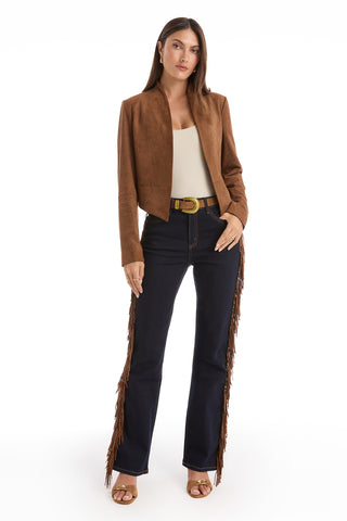 A woman faces forward, wearing a brown suede jacket, cream top, dark blue jeans with side fringe, tan heeled sandals, and the Shelly Belt - Cognac with a gold cowboy buckle, all set against a white background.
