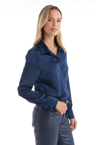 A woman with long blonde hair wears the Paulina Silk Blouse in navy, paired with matching pants, as she stands against a white background and looks slightly to the side.