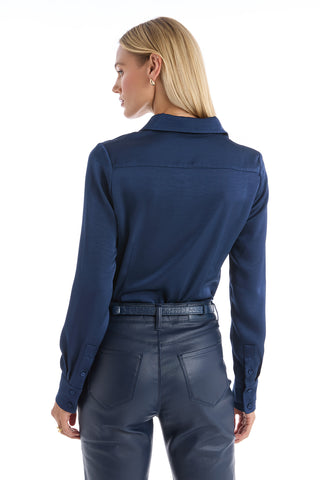 A woman with straight blonde hair is seen from the back, looking over her left shoulder in a Paulina Silk Blouse - Navy against a white background.