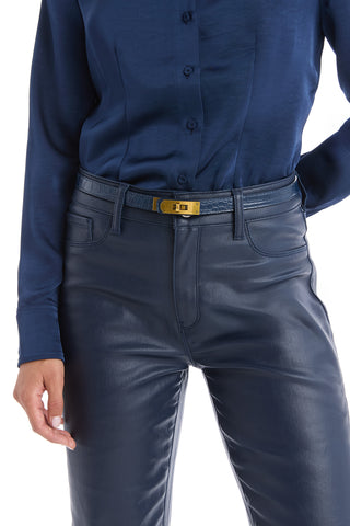 A person wears a navy button-up shirt tucked into high-waisted dark blue leather pants, paired with the Nicola Belt - Navy featuring a golden lock closure. Only the torso and upper legs are visible.