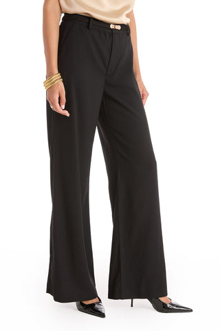 A person in Martina Belted Trouser - Black, paired with black pointed-toe heels and gold bangles on one wrist, stands against a white background.