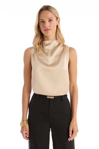 A woman with long blonde hair faces forward wearing the Mara Silky Top - Champagne, a sleeveless mock neck satin blouse, paired with black pants and gold jewelry, set against a crisp white background.