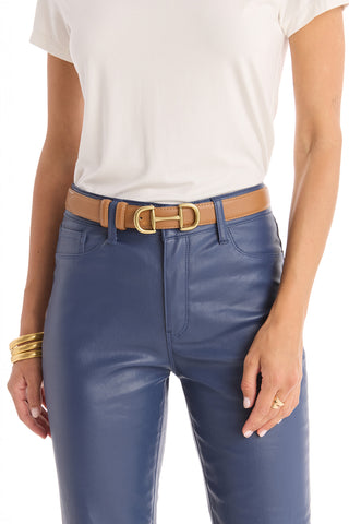 Woman wearing a white short-sleeve top tucked into high-waisted blue leather pants, accessorized with the Bettie Belt in Mocha—featuring a gold-toned buckle—and styled with gold bangles and a gold ring.