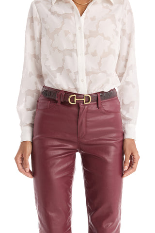 A person styles high-waisted maroon leather pants and a white floral button-up blouse with the Bettie Belt - Merlot, featuring pebbled faux leather and a striking gold-toned buckle.
