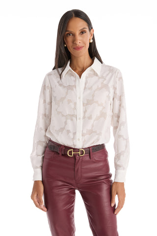 A woman wears the Stelle Button Up - White, a semi-sheer floral lace top, tucked into high-waisted burgundy leather pants with a black belt. This chic piece adds delicate style to her polished look against a white background.