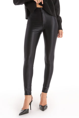 A person wearing the Suzette Skinny Pant - Black with a high-rise waist, paired with a black long-sleeve sweater and black pointed-toe heels, stands against a white background.