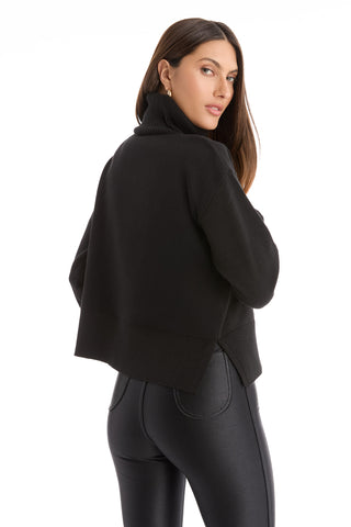 A woman with long brown hair, wearing the Gia Ultra Soft Sweater in black and fitted pants, poses turned slightly to the side against a plain white background.