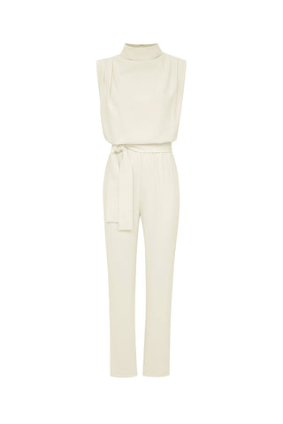 Presenting the Charli Jumpsuit - Pearl: a chic sleeveless piece in a cream hue, featuring a high neckline and a coordinating fabric belt that cinches at the waist. This slim-fit jumpsuit boasts straight-legged pants, offering a sleek and elegant silhouette set against a plain white background.