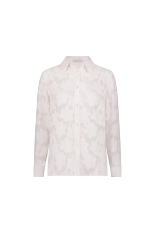 The Stelle Button Up - White is a long-sleeved, button-up blouse with a subtle abstract pattern, classic collar, and relaxed fit. Shown against a plain white background, it’s a versatile layering piece.