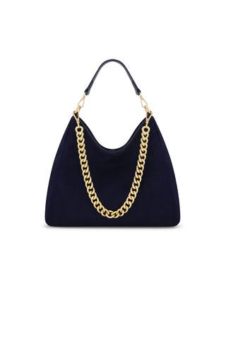 The Tribeca Chain Denim Bag - Indigo features a thick gold chain strap and a small leather handle in navy blue, displayed against a white background.