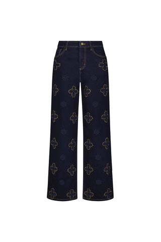 The Kaia Studded High Rise Jean in indigo features wide legs, front pockets, a gold button closure, and an all-over pattern of gold studded geometric shapes. Displayed on a white background.