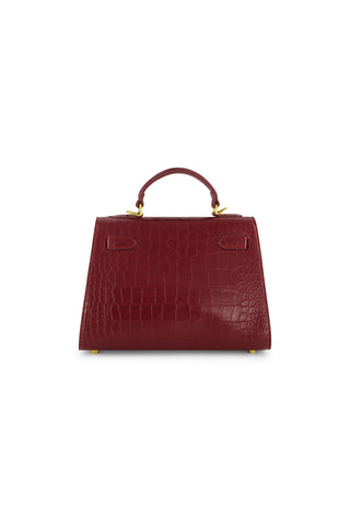 The Kayla Croco Handbag - Merlot features a structured silhouette with crocodile texture, gold hardware, and a short top handle, shown against a white background.