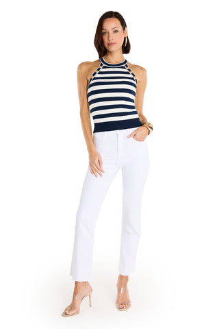 A woman poses against a white background wearing the Martha Button Halter Tank in navy stripe, paired with white pants, clear high-heeled sandals, and a gold bracelet, with one hand in her pocket.