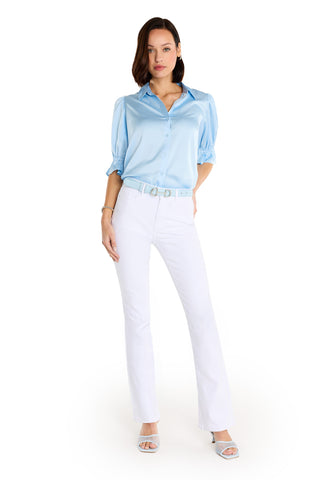 A woman with short brown hair and a neutral expression models the Cindy Ruffle Sleeve Blouse in Sky Blue, styled with white belted pants and light blue open-toe heels for a chic, feminine look against a white background.