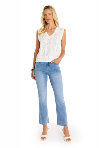A woman with long blonde hair stands against a white background wearing the Mikaela Crystal Knit Tank in white, light blue jeans, and white heeled sandals, with one hand in her pocket.